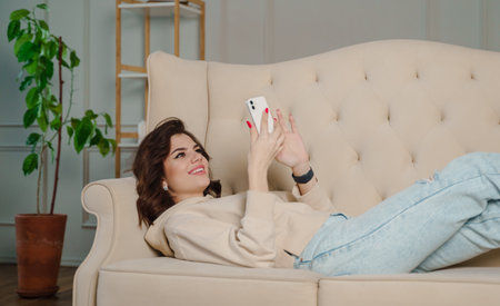 Young beautiful woman sitting on the sofa at home chatting and surfing the net. Female having fun .の写真素材