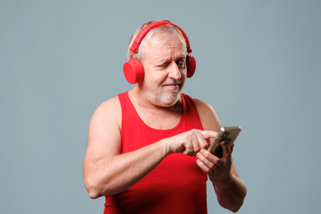 Humorous Older Male with Earphones and Smartphone, Studio Shot with Blue Backgroundの写真素材