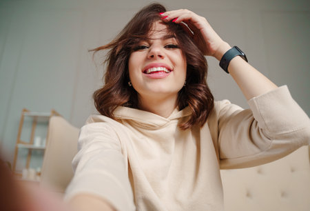 Pretty young female with big smile sitting at living room. She having fun taking selfie .の写真素材