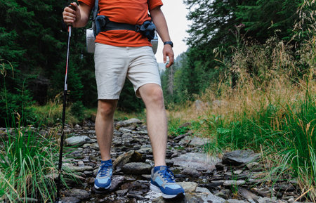Crop hiker walking down stream flowing over stones in mountainsの写真素材