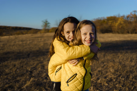 Two joyful twin sisters happily embracing in a sunlit autumn field, radiating warmth and happiness