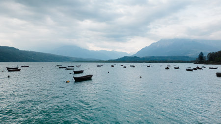 Tranquil lake, boats, mountains, cloudy sky a serene setting for relaxation and nature discoveryの写真素材