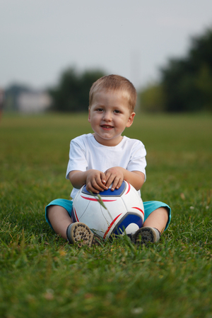 Little boy sitting on green grass with a soccer ball.の写真素材