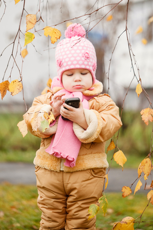beautiful little girl holding a phone on autumn park.の写真素材