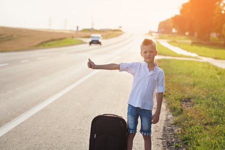 Smiling child with suitcase traveling hitchhiking. summer road   .の写真素材