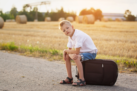 the child sits on a suitcase in the summer sunny day, the travelerの写真素材