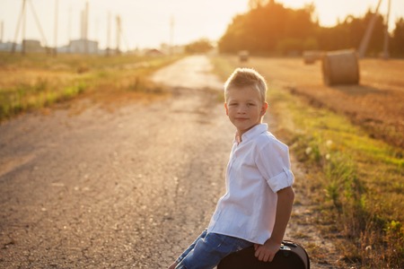 the child sits on a suitcase in the summer sunny day, the travelerの写真素材
