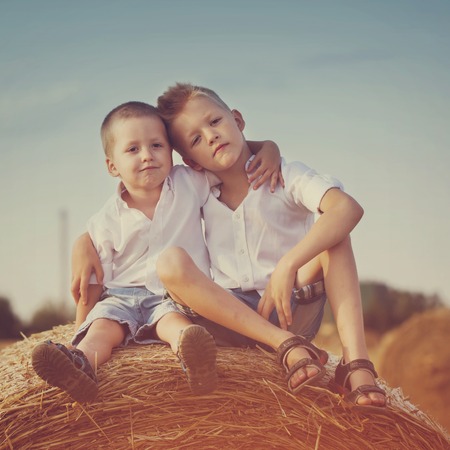 Two little brothers sitting on a haystack in wheat field on sunny summer day, toned imageの写真素材