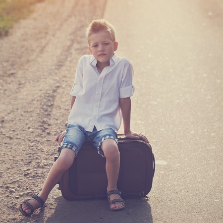 the child sits on a suitcase in the summer sunny day, the traveler,toning imageの写真素材