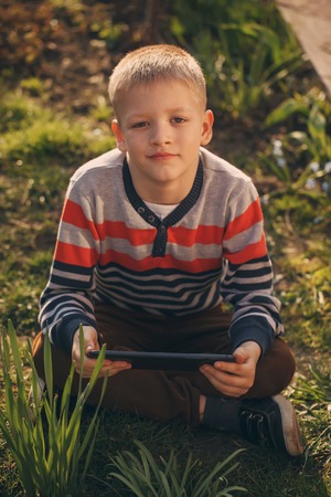 Pretty little boy with a Tablet PC on nature in early spring