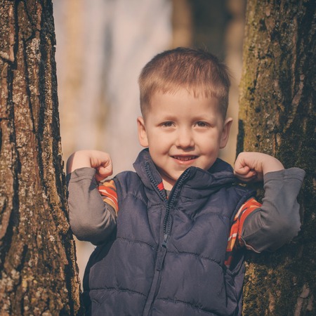 Little cute  boy in stands among the trees in sunny spring dayの写真素材