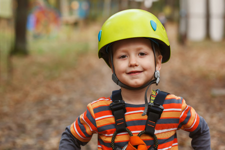 portrait of the brave smiling little boy in a helmet who is cheerfully spending time in park of adventuresの写真素材