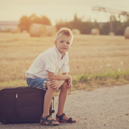 the child sits on a suitcase in the summer sunny day, the traveler. Toned imageの写真素材