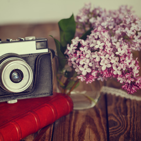 Vintage camera and Bouquet of lilac spring flowers on wooden background. Toned image. Squareの写真素材