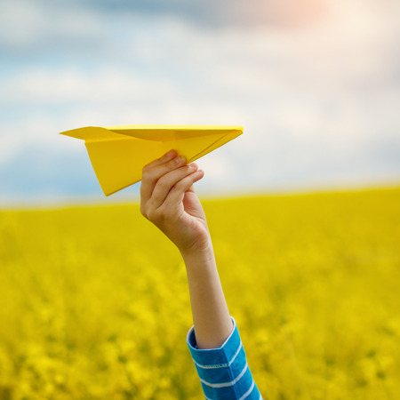 Paper airplane in children hands on yellow background and blue sky in coudy dayの写真素材