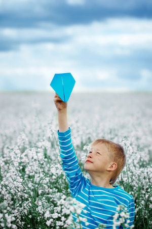 Young Boy with paper Plane against blue sky and Yellow Field Flowersの写真素材