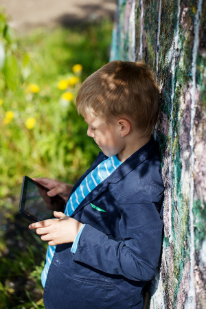 Little kid  absorbed into his tablet for educating and playing.Boy standing near a wall  graffiti.の写真素材