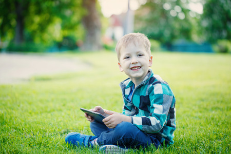 little boy with tablet sit on the grass in sunny dayの写真素材