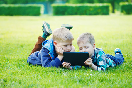 Siblings using a tablet, yingon grass in the park in suny dayの写真素材