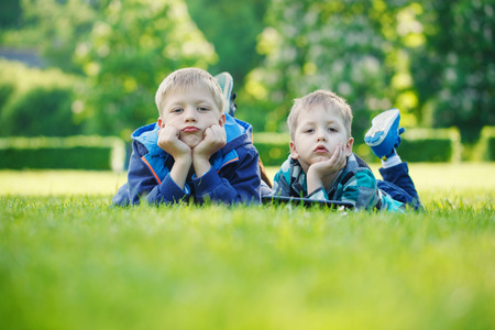 Siblings using a tablet, yingon grass in the park in suny dayの写真素材
