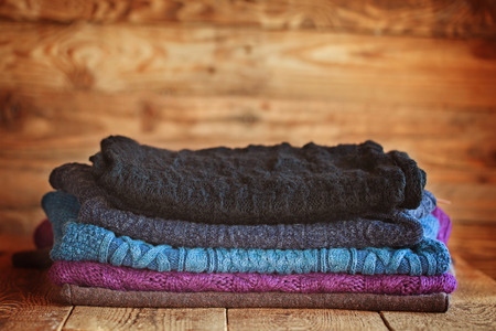 Stack of knitting colorful  warm woolen clothes on wooden wall background