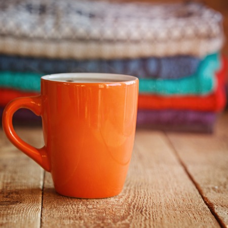 Red Cup of teaor coffee  with stack of  knitted sweaters on a wooden tableの写真素材