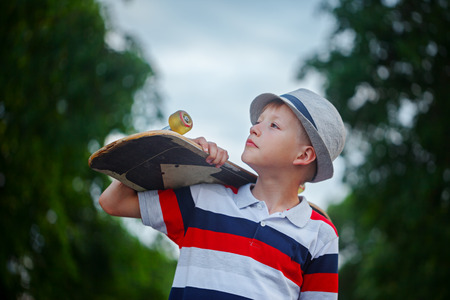 Cute boy holding skateboard  in hand outdoors.Wearing cap and stylish clothes.  Looking away.の写真素材
