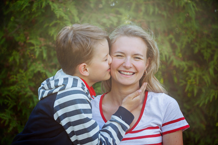 Happy little boy hugging and kissing his mother over green background. Children and happy family conceptの写真素材