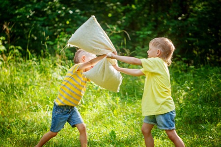 Children fighting together with pillows in a sunny summer garden. Baby boy playing in park. Pillow fightの写真素材