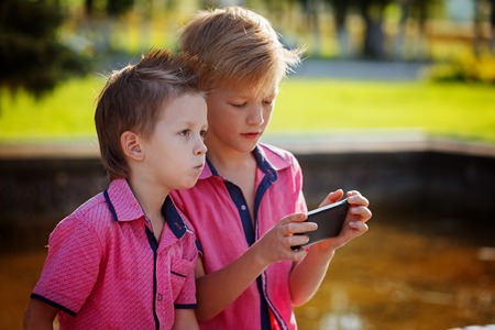 Two little boys playing games on mobile phone in sunny dayの写真素材