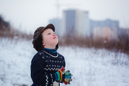 Winter portrait of little kid boy wearing a knitted sweater with deers, outdoors during snowfall....