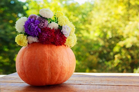 Pumpkin with colorful flowers on wooden table against natural backgroundの写真素材