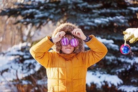 Cute boy in warm clouth and hat catching christmas ball in winter park. Kids play outdoor in snowy...