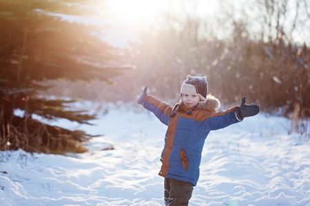 Happy little child playing throws up snow outdoors during snowfall. Active outoors leisure with children in winter on cold snowy days.の写真素材