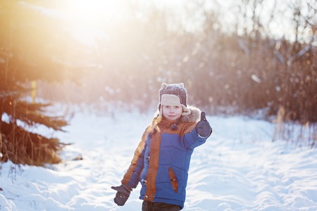 Happy little child playing throws up snow outdoors during snowfall. Active outoors leisure with children in winter on cold snowy days.の写真素材