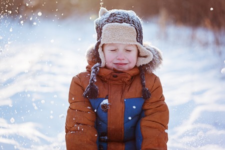 Happy child boy playing on a winter walk in nature during snowfall.の写真素材