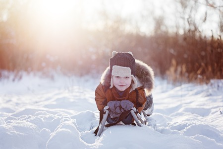 Cute little funny child boy in warm winter clothes having fun on snow sledge, outdoors during...