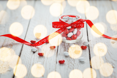 Colorful candy jar decorated with a red bow with hearts on white wooden background. Valentines day concept.の写真素材