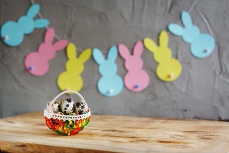 Basket with quail eggs and colorful bunnies garland on wooden background.の写真素材