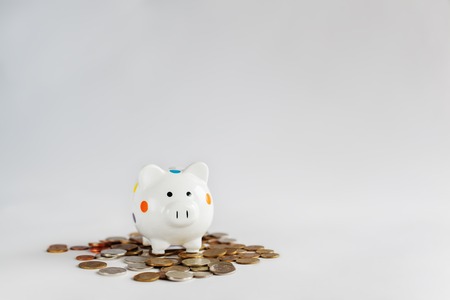 White piggy bank or money box standing on heap of money coins