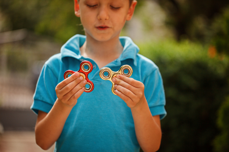 Cute little boy playing with fidget hand spinners in summer day. Popular and trendy toy for children and adultの写真素材