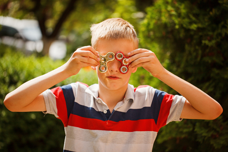 Schoolboy playing with fidget hand spinners in summer day. Popular and trendy toy for children and adultの写真素材