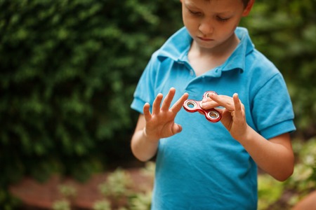 Cute little boy playing with fidget hand spinner in summer day. Popular and trendy toy for children and adultの写真素材