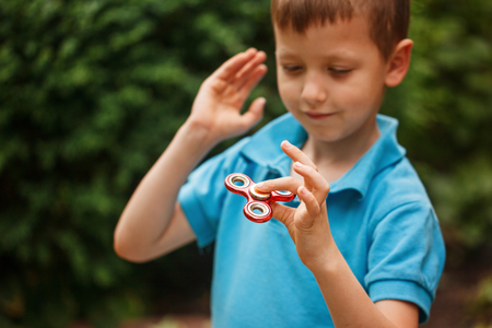 Cute little boy playing with fidget hand spinner in summer day. Popular and trendy toy for children and adultの写真素材