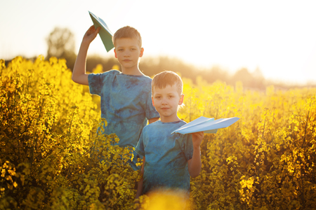 Two little boys friends with blue paper plane in summer yellow field. Brother love. Concept friendshipの写真素材
