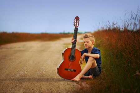 Teenage boy with acoustic guitar on country road