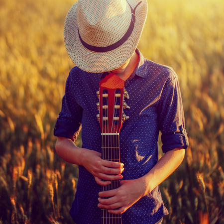 Teenage boy in hat with acoustic guitar on sunset, outside. Toning imageの写真素材