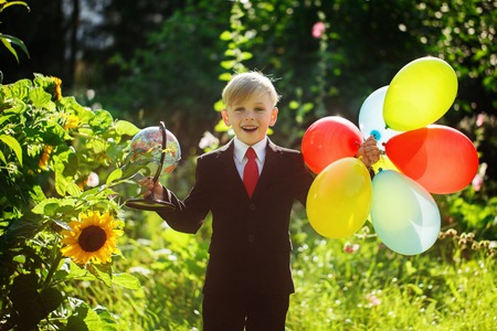 Cute boy smiling, going back to school. Boy in the suit. Child with globe and colorful balloons on first school dayの写真素材