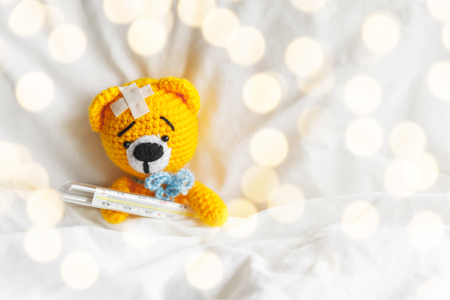 Yellow teddy bear with thermometer and plaster on head in white bedroomの写真素材