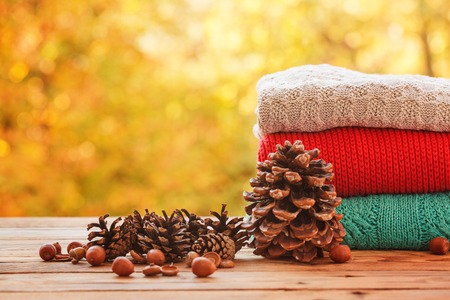 Stack pile of cozy colorful knitted sweaters on autumn nature background. Concept warm clothing.の写真素材